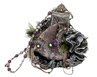 May include: A grey velvet pouch bag featuring a silver metal frame with a decorative clasp. The bag is adorned with purple beads, green feathers, sequins, and dangling beaded fringe. A long beaded handle with purple and green accents is attached.
