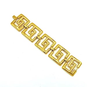 May include: A gold-toned bracelet with a geometric design. The bracelet features a series of interconnected square links, each with a repeating Greek key pattern. The links are connected by small hinges, and the bracelet has a clasp closure.