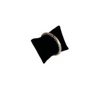 May include: A silver bangle bracelet with an ornate floral design. The bracelet is displayed on a black velvet pillow against a white background. The bracelet appears to be approximately 2.5 inches in diameter.
