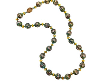May include: A vintage necklace featuring ornate, round beads with a floral design in shades of green, red, and gold. The beads are strung on a green cord with gold-colored spacers and a decorative clasp. The necklace is a statement piece.