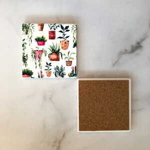 May include: Square ceramic coaster with a white background and a repeating pattern of potted plants in various colors. The coaster has a cork backing and a white border.