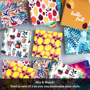 May include: A collection of square ceramic coasters with various designs, including botanical, lemon, and fall-themed patterns. One coaster features the text "hello fall." The coasters are designed to be mixed and matched.