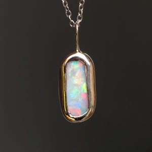 May include: A silver pendant necklace featuring a rectangular opal gemstone. The opal displays a play of color with iridescent hues of pink, green, and blue. The pendant is suspended from a delicate silver chain.