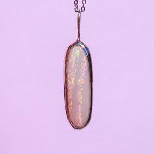 May include: A silver chain necklace with a white opal pendant. The opal is oval shaped and has a iridescent sheen.