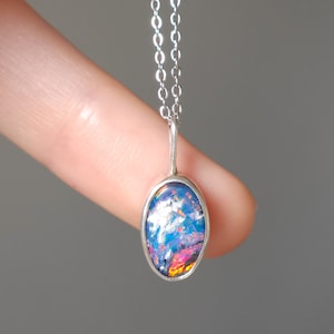 May include: A silver chain necklace with a silver oval pendant featuring a blue, pink, and orange opal.