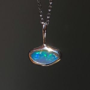 May include: A silver pendant necklace featuring an oval-shaped opal gemstone with vibrant blue and green flashes of color. The stone is set in a smooth, polished silver bezel with a simple bail attached to a delicate silver chain link necklace.