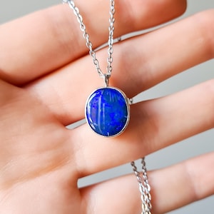 May include: A silver chain necklace with a blue opal pendant. The pendant is round and has a smooth, polished surface.
