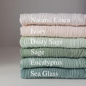 Op de afbeelding: Stapel van zes linnen stofstalen in verschillende tinten groen en crème. De staal zijn gelabeld met "Natuurlijk linnen", "Ivoor", "Stoftige Salie", "Salie", "Eucalyptus" en "Zeeglas".