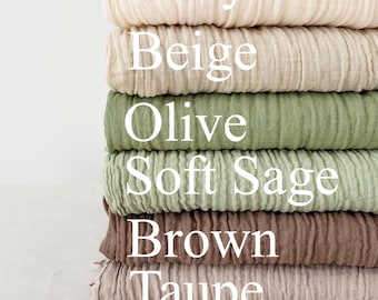 May include: A stack of six folded fabric swatches in various neutral colors. The colors include ivory, beige, olive, soft sage, brown, and taupe. The names of the colors are printed on the fabric.