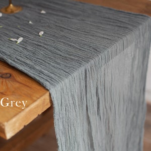 Puede incluir: Un camino de mesa de lino gris con una superficie texturizada y arrugada. El camino de mesa está colocado sobre una mesa de madera.