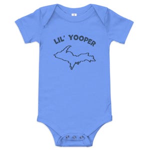 Peut inclure: Un body pour bébé bleu clair à manches courtes avec un contour bleu foncé de la péninsule supérieure du Michigan et le texte LIL' YOOPER imprimé en bleu foncé au-dessus de la carte. Le vêtement possède un col rond et trois boutons-pression.