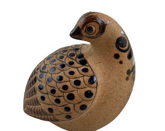 Puede incluir: Una figurita de pájaro de cerámica pintada a mano con detalles en marrón, azul y blanco. El pájaro tiene un cuerpo redondeado y un diseño detallado.