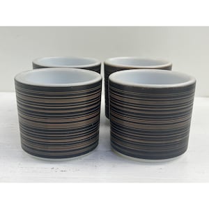 Puede incluir: Juego de cuatro tazas de cerámica blanca con diseños de rayas negras y marrones.