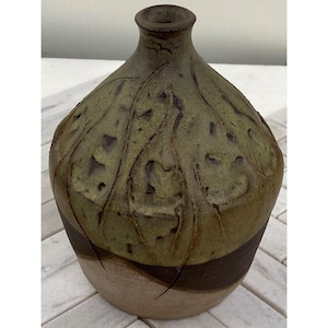 Può includere: Un vaso in ceramica verde e marrone con una superficie testurizzata. Il vaso ha una base larga e un collo stretto.