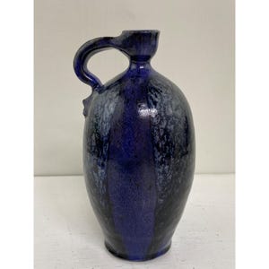 Könnte beinhalten: Ein blauer und schwarzer Keramik Krug mit einem einzigartigen Henkel. Der Krug hat eine gesprenkelte Glasur und einen runden Körper.