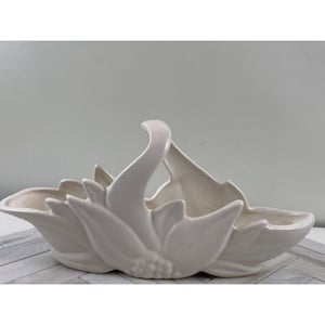 May include: A white ceramic flower-shaped basket with a handle. The basket is designed to look like a stylized flower with leaves and a center.