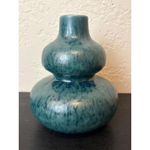 Op de afbeelding: Een turquoise keramische vaas met een bolvormige body en een smalle hals. De vaas heeft een getextureerd oppervlak en een glanzende afwerking. Het ontwerp doet denken aan een kalebasvorm, geschikt voor interieurdecoratie.