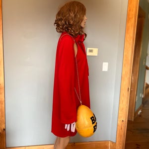 May include: A vibrant red dress with a matching bow and a gold chain strap. The dress is paired with a yellow and black purse. The purse has the letters "BEE" printed on it.