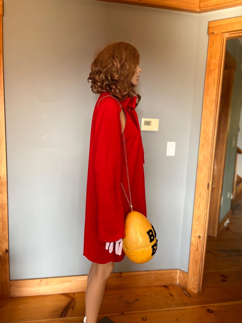 May include: A vibrant red dress with a matching bow and a gold chain strap. The dress is paired with a yellow and black purse. The purse has the letters "BEE" printed on it.