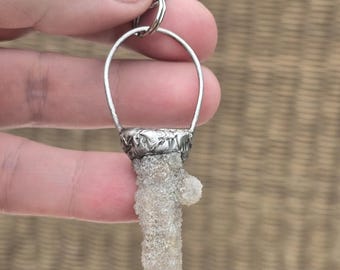 May include: A silver keychain with a clear crystal charm shaped like a jagged icicle. The crystal is attached to a silver ring and a silver chain with a lobster clasp.