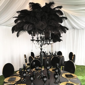 May include: Black and gold table setting with black velvet chairs and a black candelabra with black ostrich feathers.