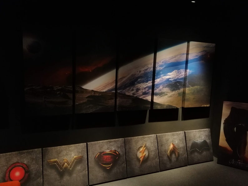 May include: A wall display of six framed images of space scenes, including a planet, a nebula, and a star field. Below the images are nine smaller framed images of superhero logos, including Superman, Wonder Woman, Batman, and The Flash.