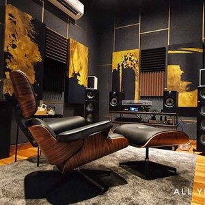May include: A home theater room with black and gold walls, a brown leather armchair, a footrest, and a large speaker system. The room is decorated with abstract paintings.
