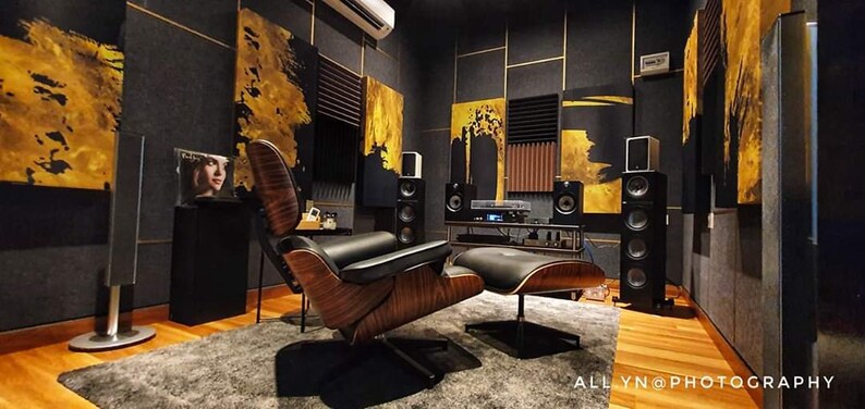 May include: A home theater room with black and gold walls, a brown leather armchair, a footrest, and a large speaker system. The room is decorated with abstract paintings.