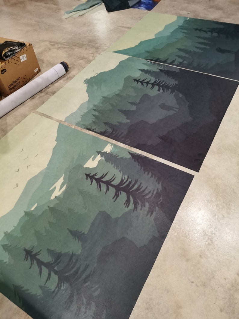 May include: Three different sized prints of a forest scene with mountains in the background. The prints are in shades of green and blue, with a light yellow sky. The prints are arranged in a staggered pattern.