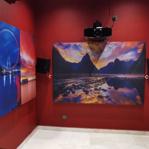 May include: Four framed canvas prints with different scenic images. The prints are hung on a red wall. The images include a city skyline, a Ferris wheel, a mountain range, and a body of water.