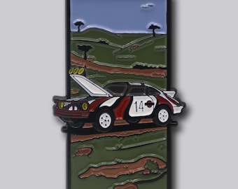 May include: Enamel pin featuring a vintage race car with the number 14, in red, white, and black. The car has its hood open, set against a backdrop of a green landscape and blue sky. The pin is rectangular with a black border.