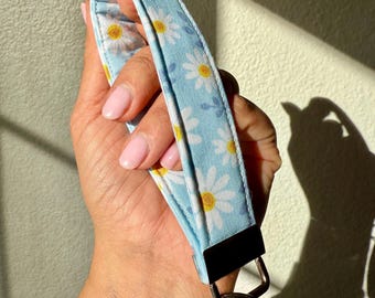 Könnte beinhalten: Ein blauer und weißer Blumen-Schlüsselanhänger mit einem silbernen Schlüsselring. Der Schlüsselanhänger ist aus Stoff mit einem Gänseblümchenmuster.