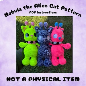 May include: Three crocheted alien cat dolls with large eyes and antennae. The left is neon green with a black collar, the center is dark blue with white stars, and the right is neon pink with a black collar. Text reads: Nebula the Alien Cat Pattern PDF instructions NOT A PHYSICAL ITEM.