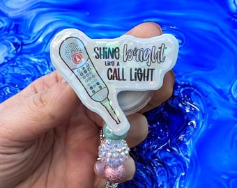 May include: A white and silver phone-shaped badge reel with the text "Shine bright like a call light". The reel is attached to a beaded chain with pink, white, and blue beads.