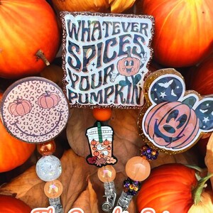 May include: A set of three pumpkin spice themed retractable badge holders with charms. The charms include a pumpkin with a face, a pumpkin with a Mickey Mouse head, and a Starbucks cup with a pumpkin on it. The text on the badge holder says "Whatever Spices Your Pumpkin".