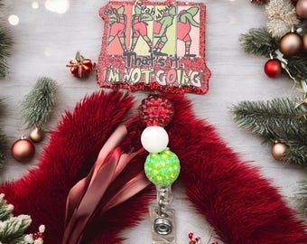 Könnte beinhalten: Ein rotes Glitzer-Badge-Rollo mit dem Text "That's it, I'm not going" und einem Cartoon-Bild von Personen. Das Rollo ist mit einem roten, flauschigen Schal und Weihnachtsdekorationen kombiniert.
