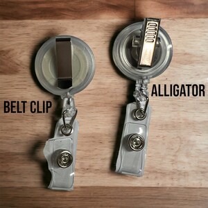 May include: Two clear plastic retractable badge holders with a silver belt clip and a gold alligator clip. The text "BELT CLIP" is printed on the left holder and "ALLIGATOR" is printed on the right holder.
