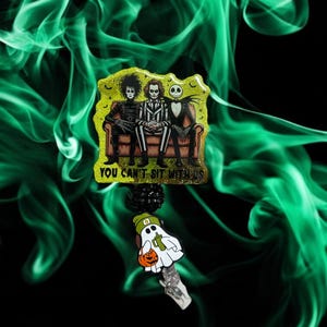 May include: A Halloween-themed badge reel featuring Edward Scissorhands, Beetlejuice, and Jack Skellington on a couch, with the text "YOU CAN'T SIT WITH US." A ghost with a pumpkin and a green hat is also included.