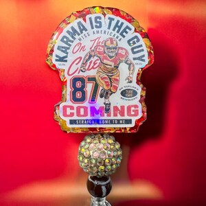 May include: A red, white and gold resin keychain with a football player graphic and the text "Karma is the guy, Miss Americana, On the Chiefs, 87, Go Taylor's Team 1989 Boyfriend, Coming, Straight Home to Me".