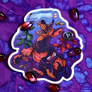 May include: A sticker featuring a cartoon illustration of a black and orange dog with a red, white, and blue background. The dog is snarling and has a red, white, and blue ribbon around its neck. The sticker also features a small black and white circle with the text "Ink Ribbon" on it.