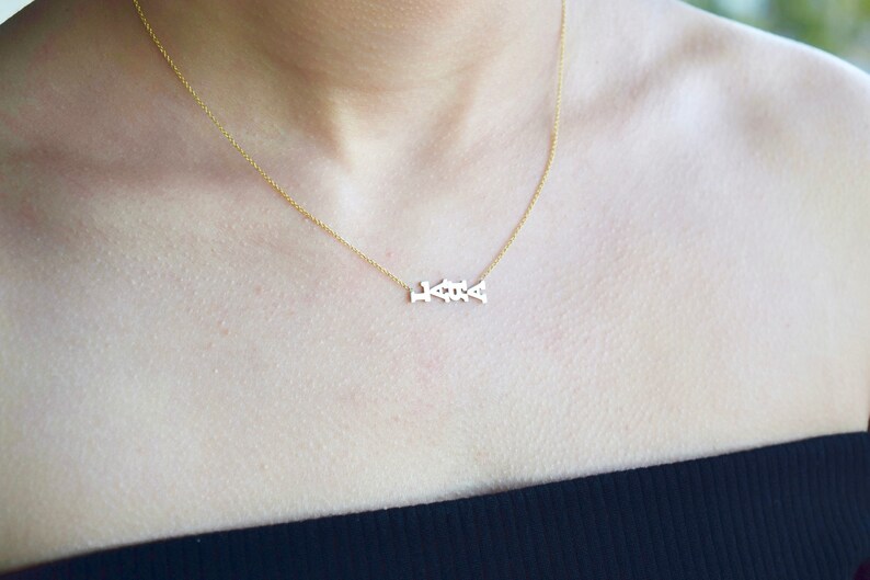 Puede incluir: Un collar de cadena de oro con un delicado colgante que deletrea la palabra "Love".