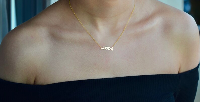 Puede incluir: Un collar de oro con una cadena delicada y un peque&ntilde;o colgante que dice "LOVE" en cursiva.