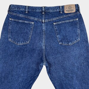 Pu&ograve; includere: Un paio di jeans blu denim con una toppa in pelle marrone sul retro che dice "Wrangler" in lettere bianche.