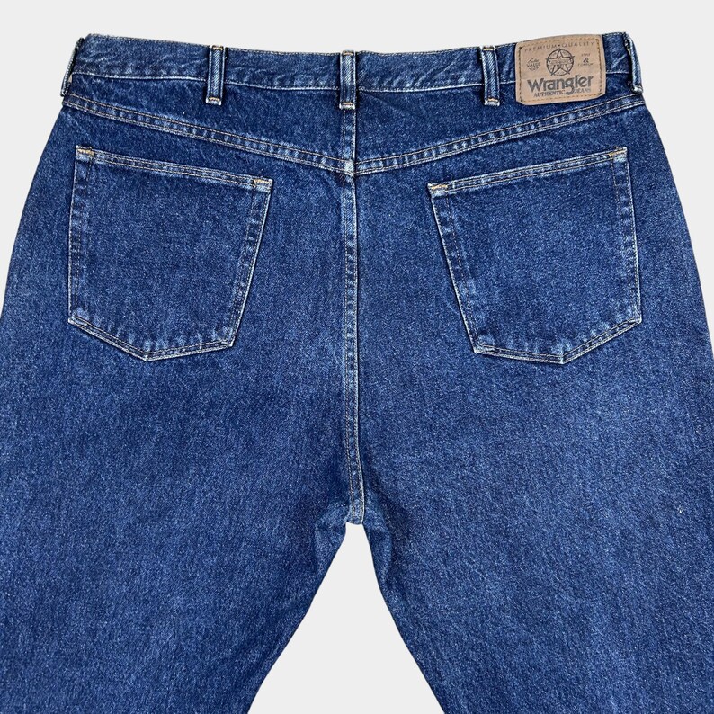 Pu&ograve; includere: Un paio di jeans blu denim con una toppa in pelle marrone sul retro che dice "Wrangler" in lettere bianche.