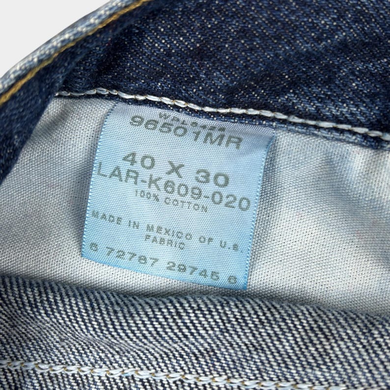 Pu&ograve; includere: Un'etichetta in denim blu con testo bianco che recita "96501MR", "40 X 30", "LAR-K609-020", "100% COTONE", "PRODOTTO IN MESSICO CON TESSUTO U.S.", "672787 29745 0".