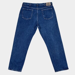 Pu&ograve; includere: Un paio di jeans blu denim con una toppa in pelle marrone sul retro della cintura che dice "Wrangler".