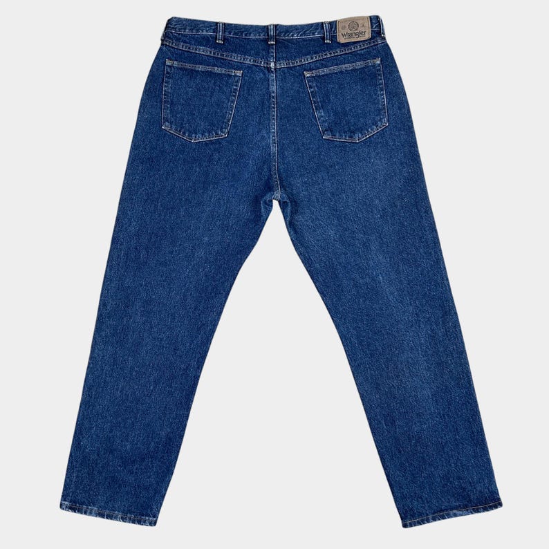 Pu&ograve; includere: Un paio di jeans blu denim con una toppa in pelle marrone sul retro della cintura che dice "Wrangler".