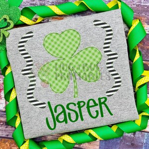 May include: A gray t-shirt with a green shamrock design and the name "Jasper" in green lettering.