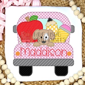 Op de afbeelding: Een roze en grijs appliqué-ontwerp van een schoolbus met een hond, een appel en een potlood erin. De bus heeft de naam "maddison" op de achterkant.