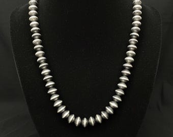 May include: A silver beaded necklace displayed on a black mannequin. The necklace features a series of round, silver beads strung together. The beads are evenly spaced and have a polished finish, reflecting light. The necklace is a classic piece of jewelry.